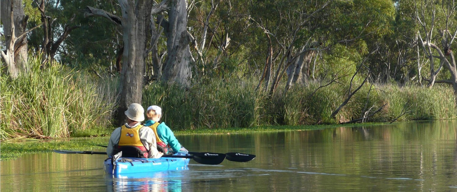 Calm water on the river Murray with two people in a blue canoe